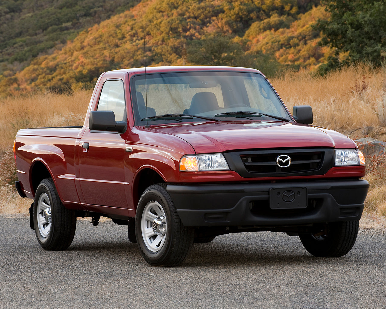 Red Mazda B2300 truck parked on the road in front of a mountain covered with yellow flowers and dry grass