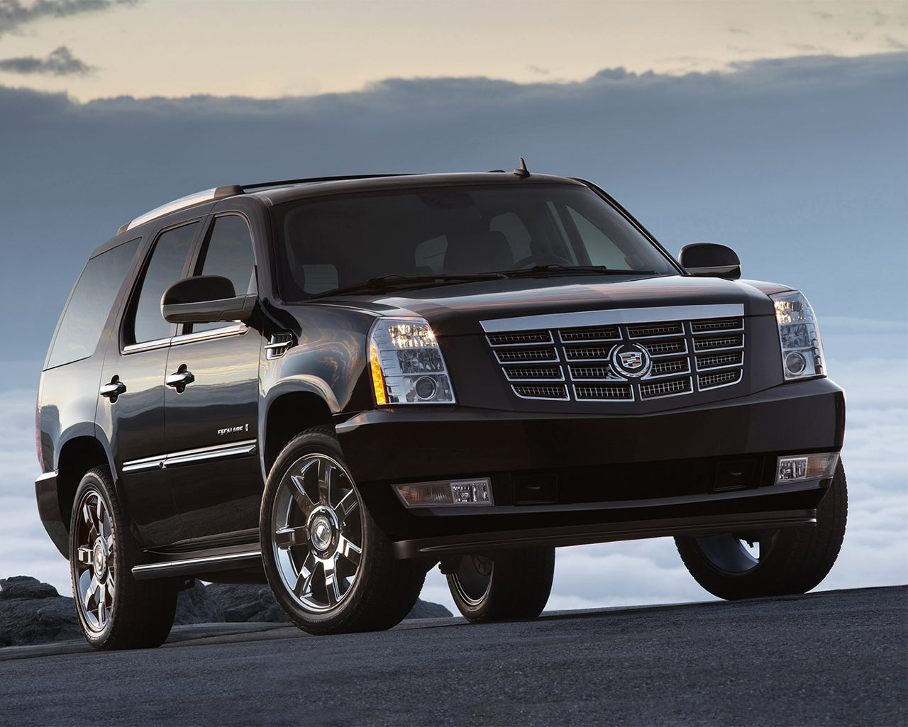 Black Cadillac Escalade parked on asphalt road with cloudy sky behind it