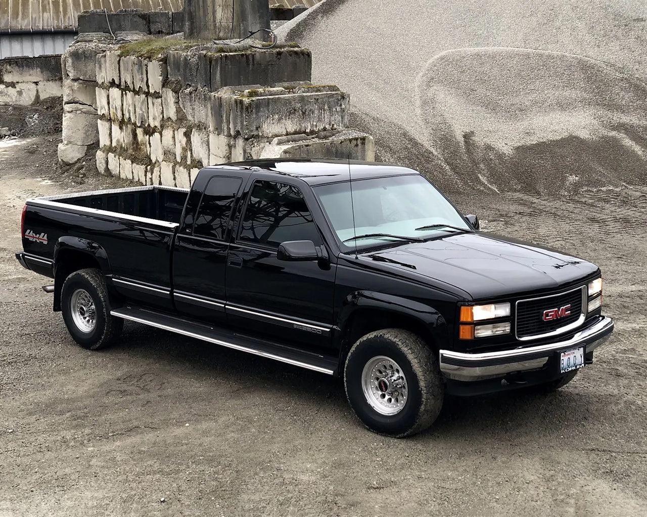 Black GMC C2500 parked in a construction zone, with brick concrete and a mound of rocks in the background