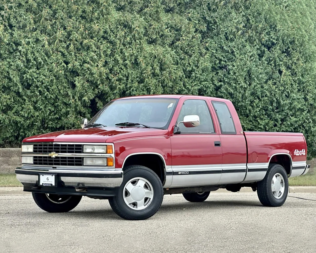 Red Chevy K1500 truck parked in front of a tree line