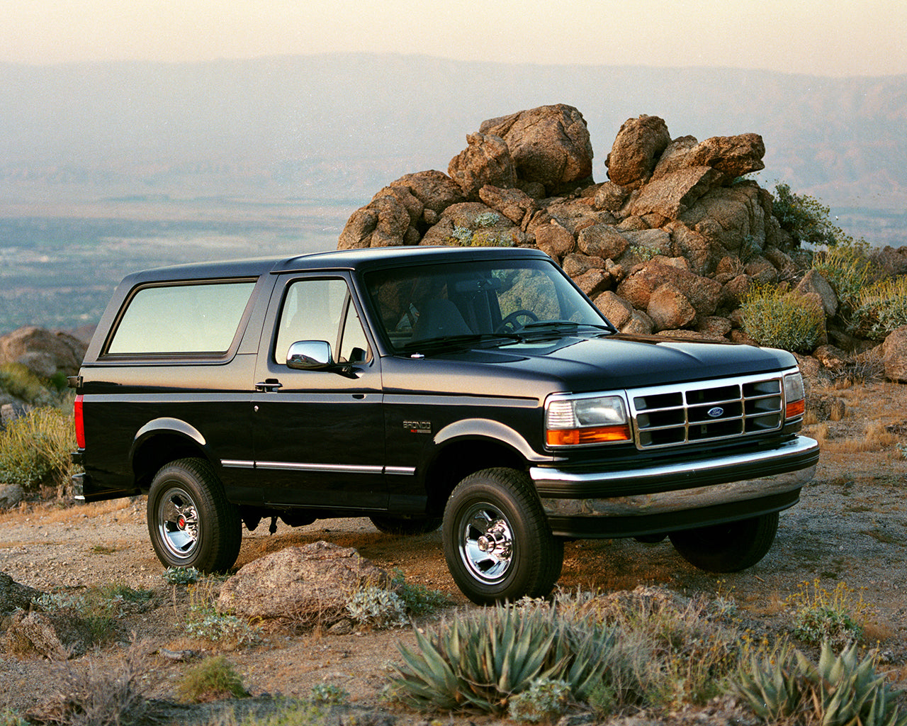 Black Ford Bronco parked on a cliff in front of a mound of rocks and a mountain range