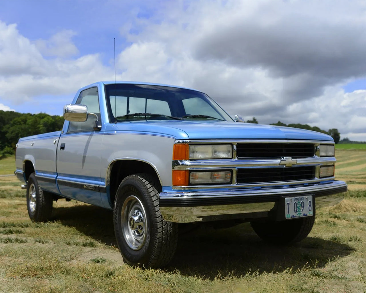 Silver and Blue Chevrolet C2500 truck parked on the grass with cloudy blue sky