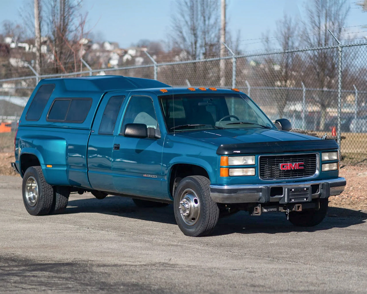 Green GMC K3500 dually parked infront of a barbed wire fence
