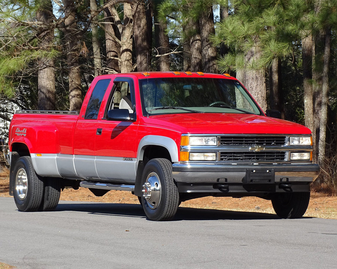 Red Chevrolet C3500 truck parked next to large trees