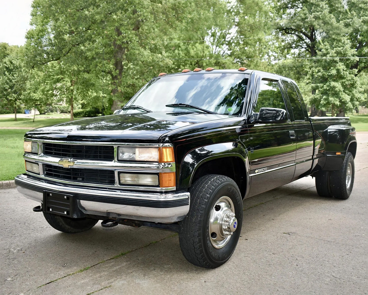 Black K3500 dually Truck parked on a street with trees behind it
