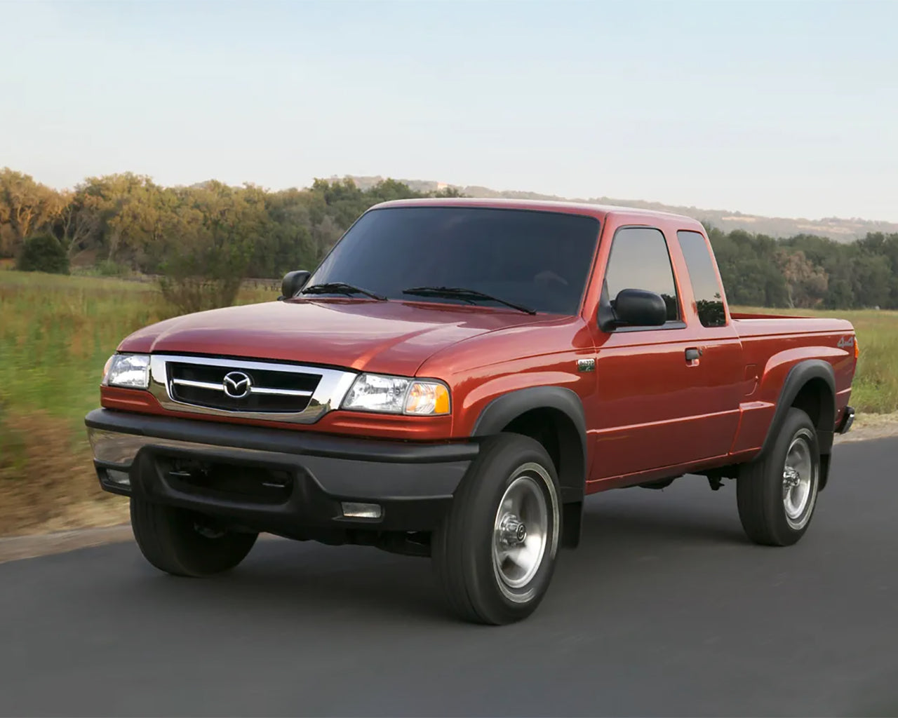 Red Mazda B4000 truck driving on a road passing a grassy field
