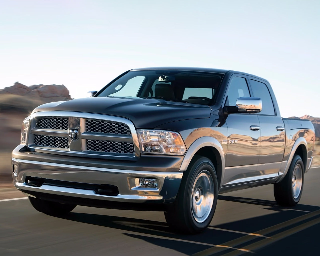 Grey Dodge Ram 1500 driving on roadway passing huge rocks behind it