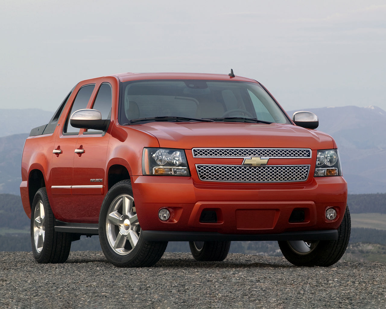 Red Chevrolet Avalanche parked on a gravel road with mountains in the background