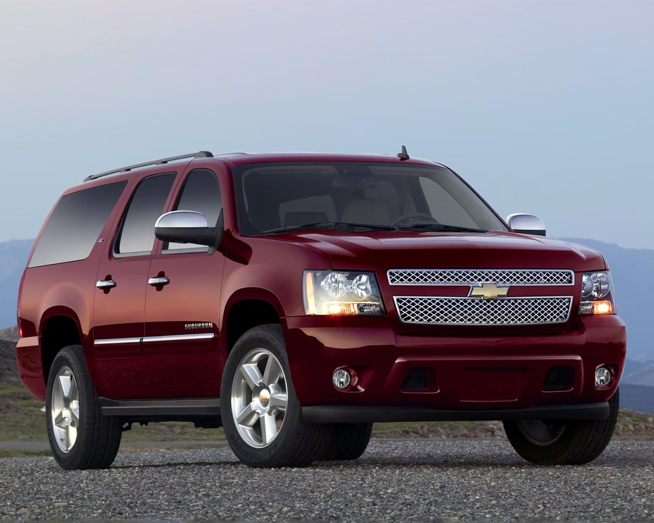 Red Chevy Suburban 1500 parked on gravel road with light blue sky in background