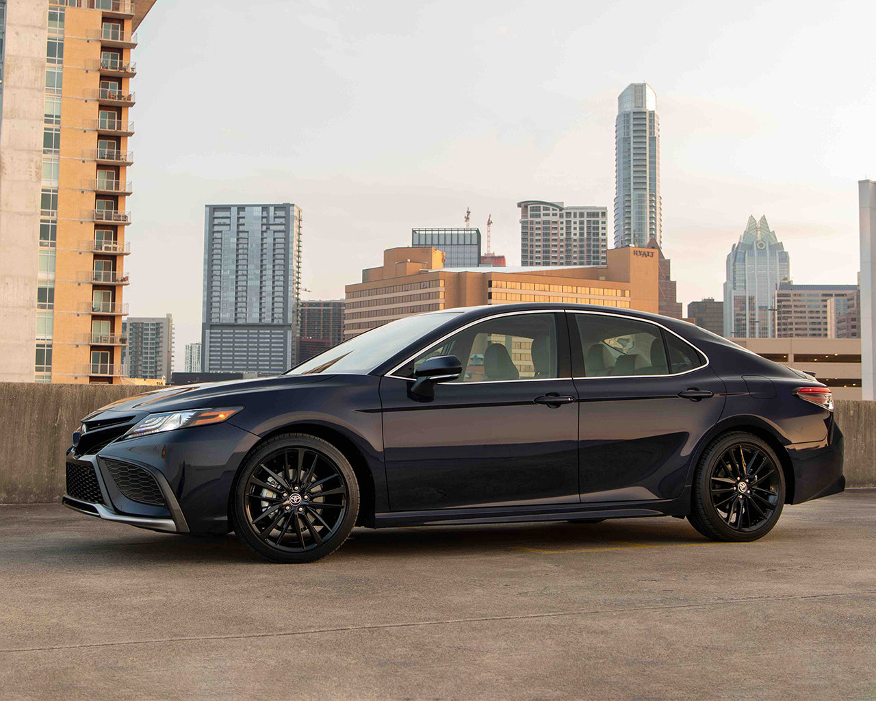 Black Toyota Camry parked on the top of a parking garage, city skyline behind it