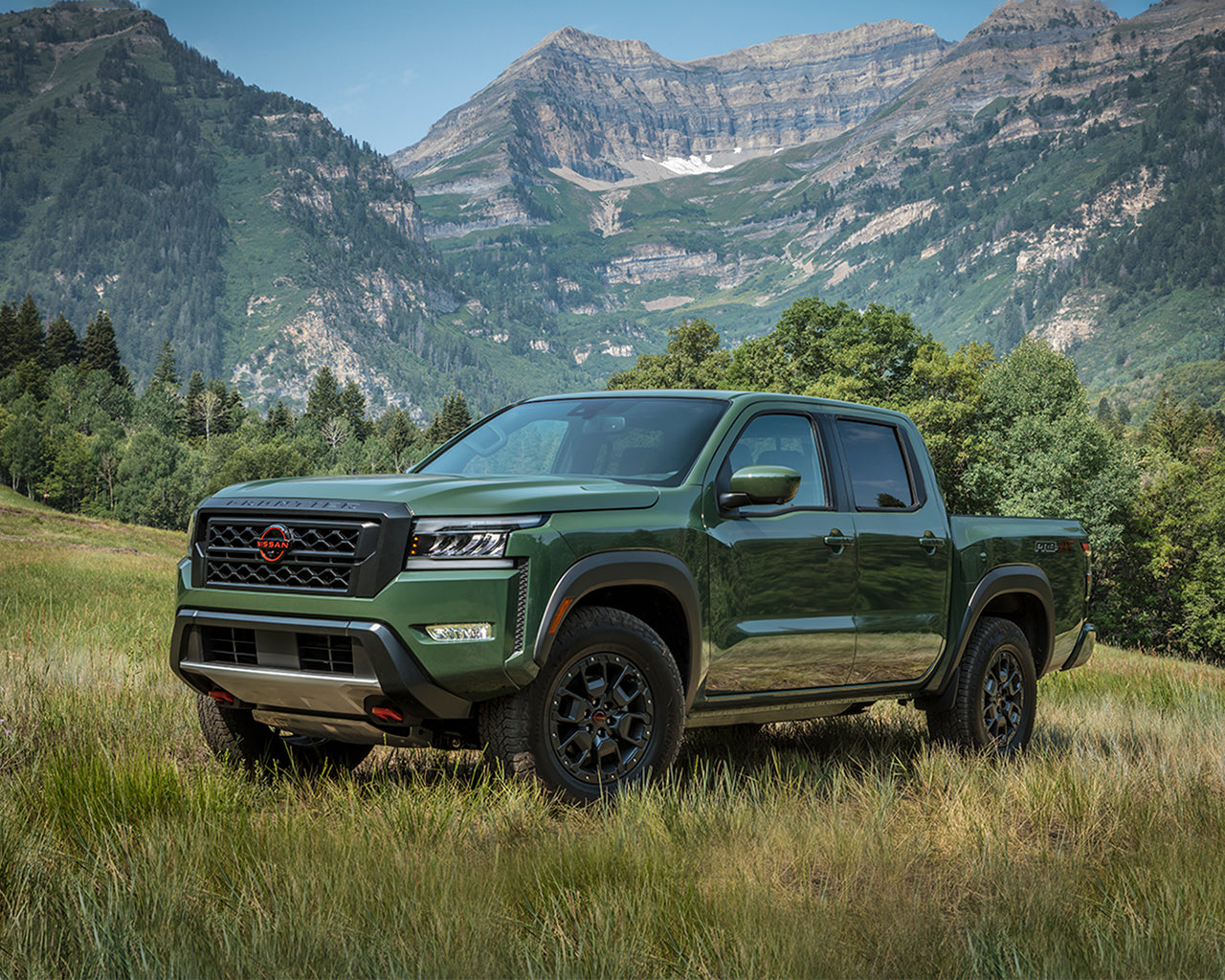 Green Nissan Frontier parked on a grassy field and large mountains behind it