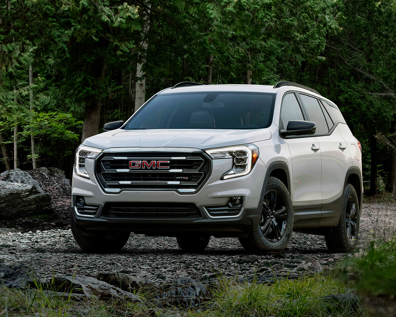 White GMC Terrain parked on rocks infront of a green forest
