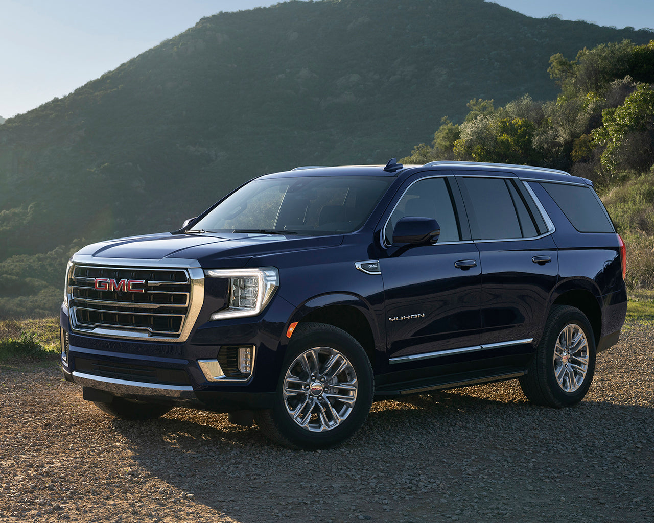 Blue GMC Yukon SUV parked on rocks with a mountain behind it