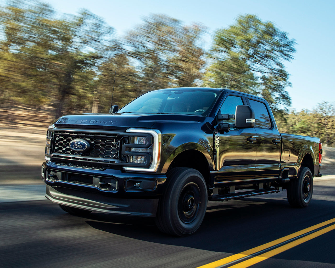 Black Ford Super Duty F-250 driving on a road with yellow divider and trees passing in the background