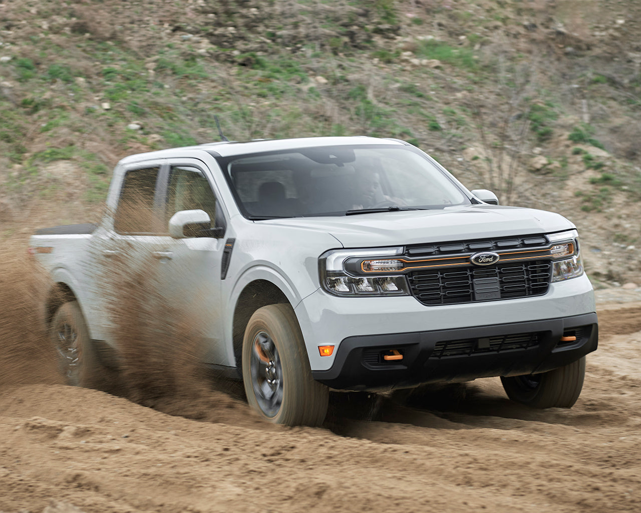Grey Ford maverick driving through loose dirt and kicking it into the air