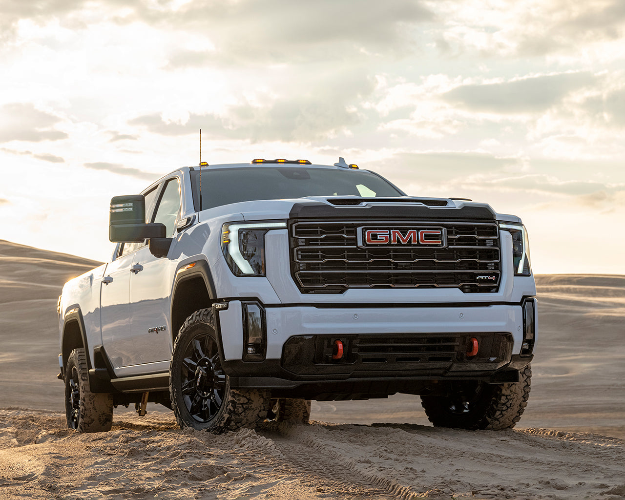 White GMC Sierra HD parked on a mound of sand, with the sun setting behind the car 