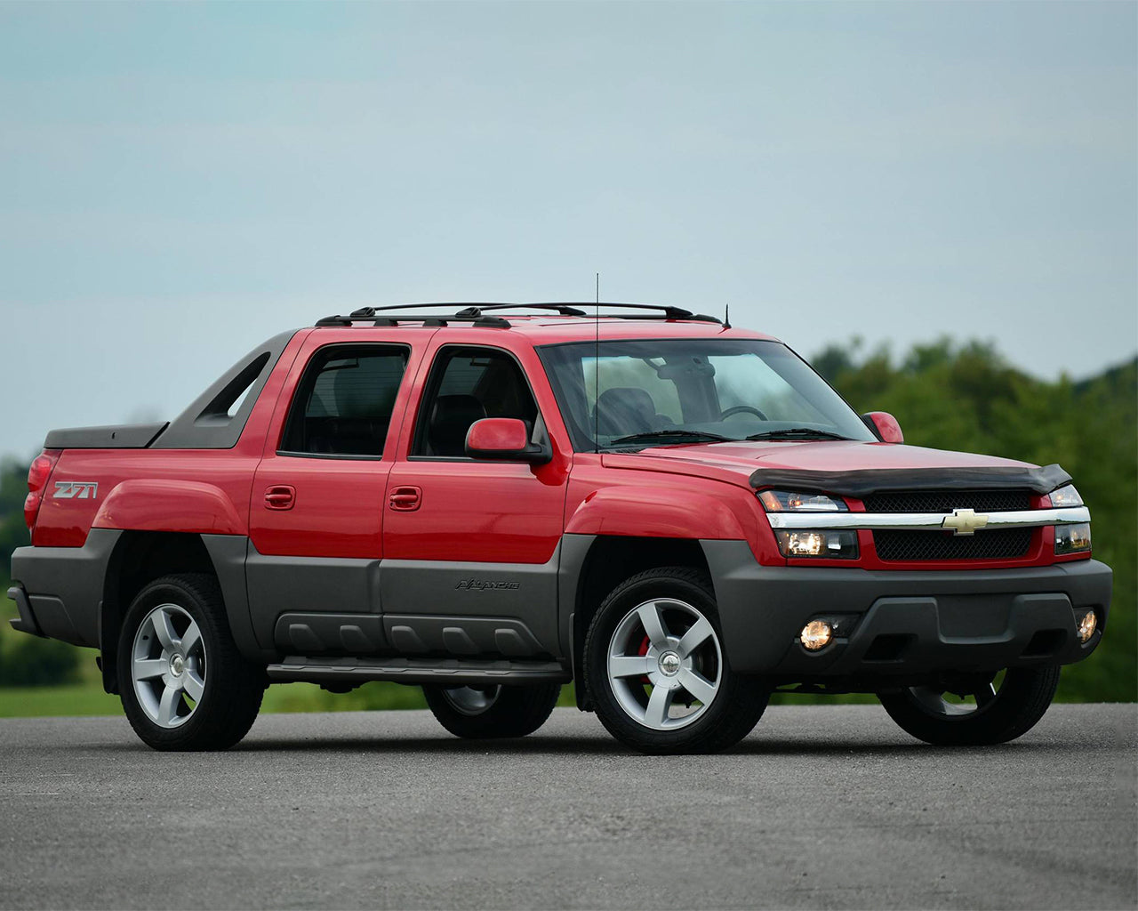 Red Chevrolet Avalanche 1500 Parked on the road in front of some trees and a blue sky