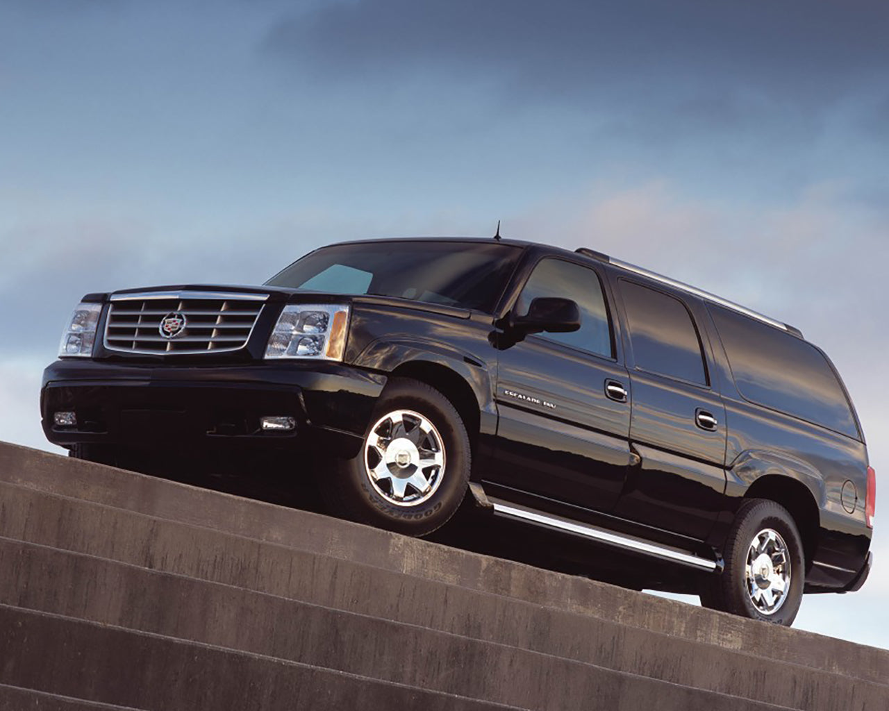 Black Cadillac Escalade ESV parked on a brick building grey clouds behind the car