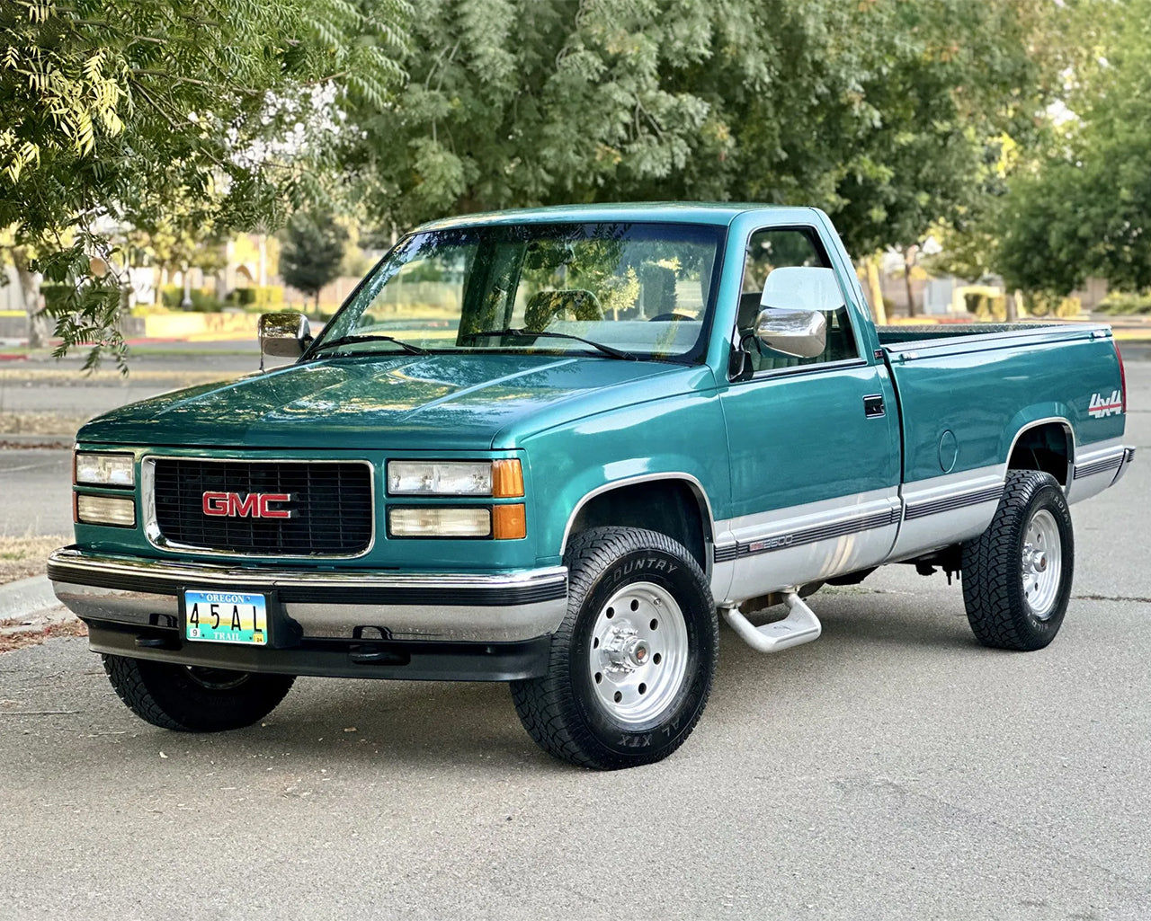 Green GMC K2500 truck parked infront of trees 