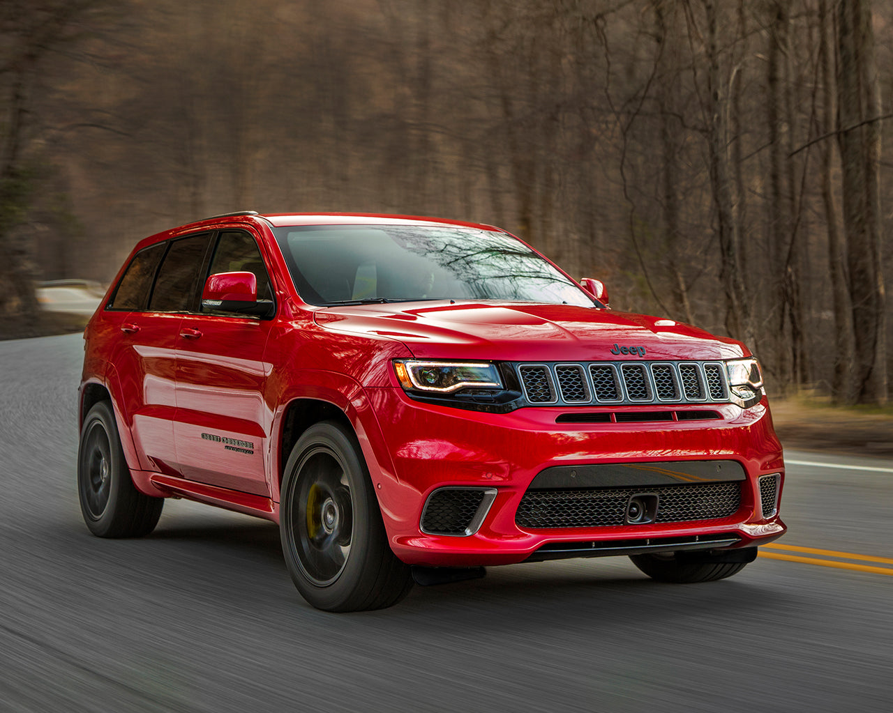 Red Jeep Grand Cherokee Trackhawk driving through forest 