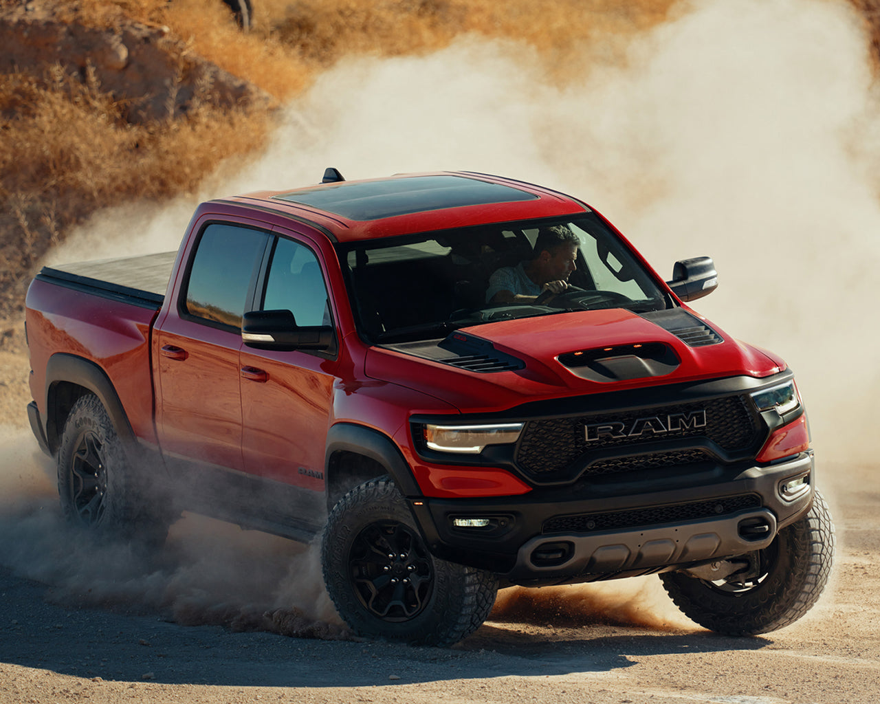 Red RAM 1500 TRX turning hard in the dirt, man behind the wheel