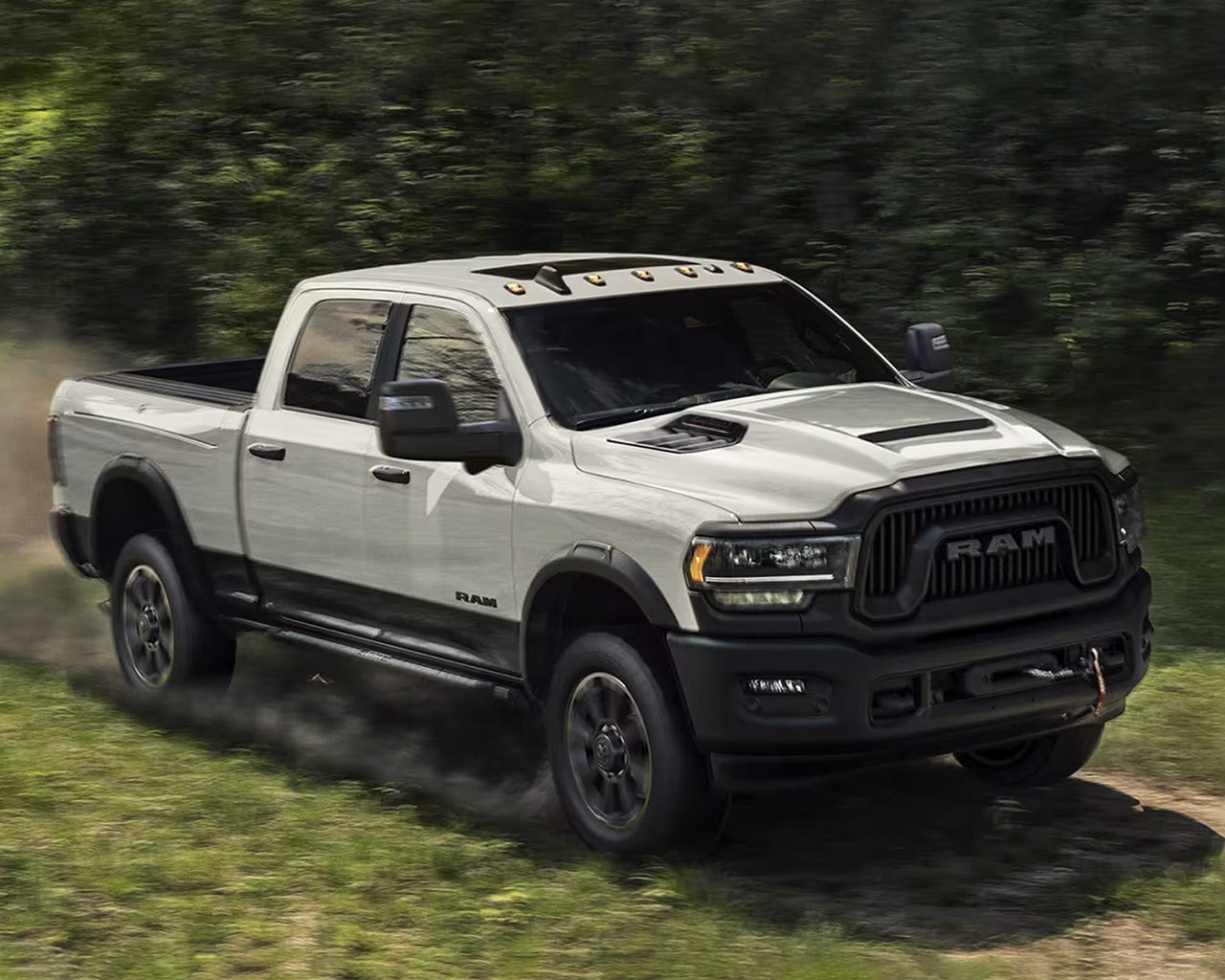 White RAM 2500 driving through a grassy path passing trees in background